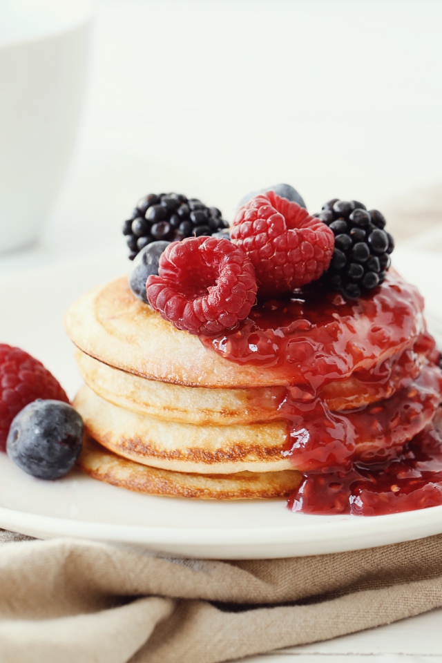 Оладьи на большой белой тарелке с джемом и ягодами 