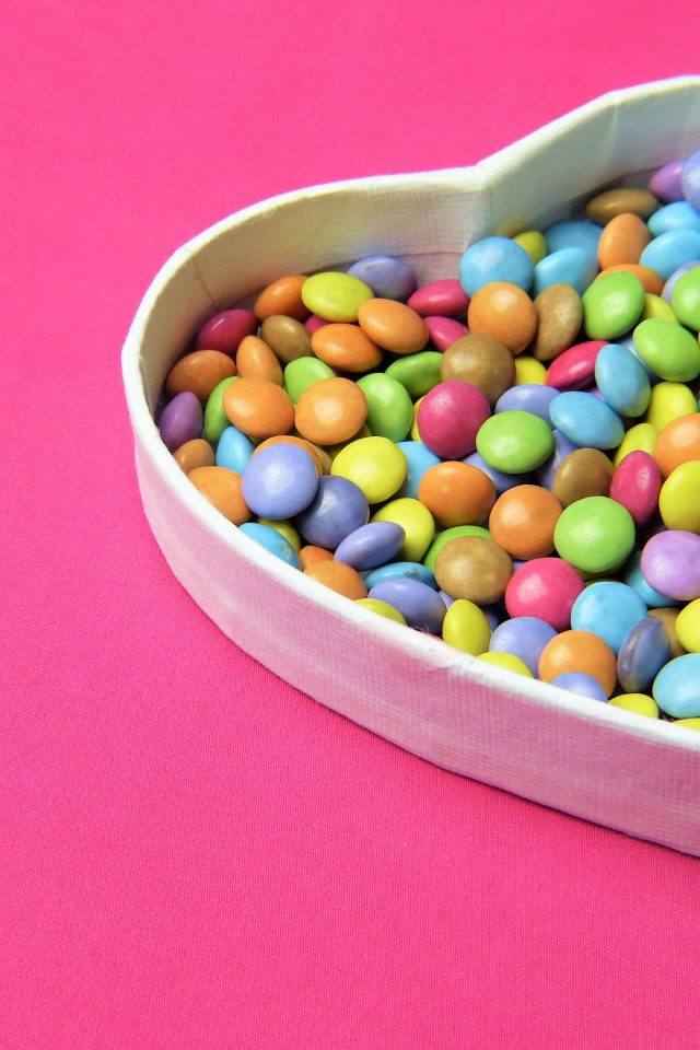 Коробка в форме сердца с разноцветными конфетами на розовом фоне