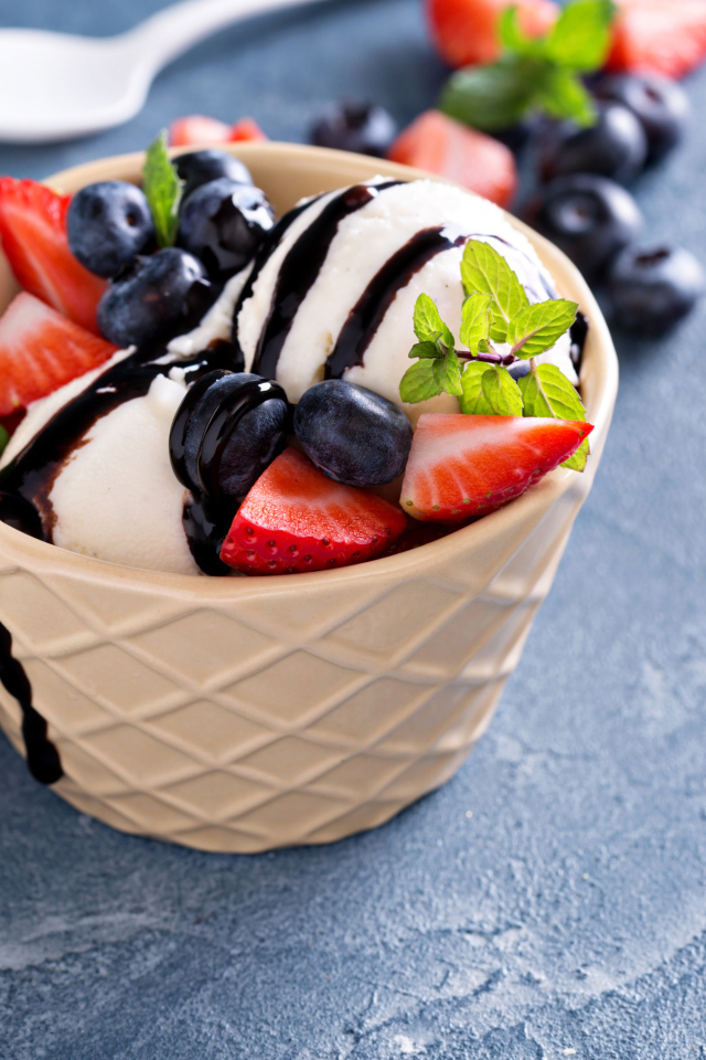 Шарики мороженого в стакане на столе с клубникой и ягодами черники