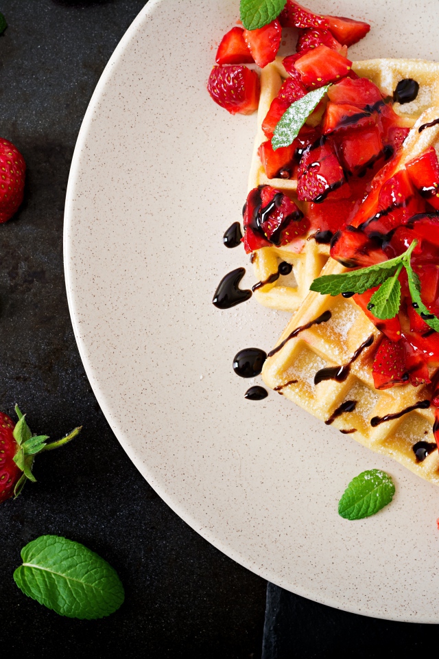 Большие вафли с ягодами клубники и шоколадом на белой тарелке 