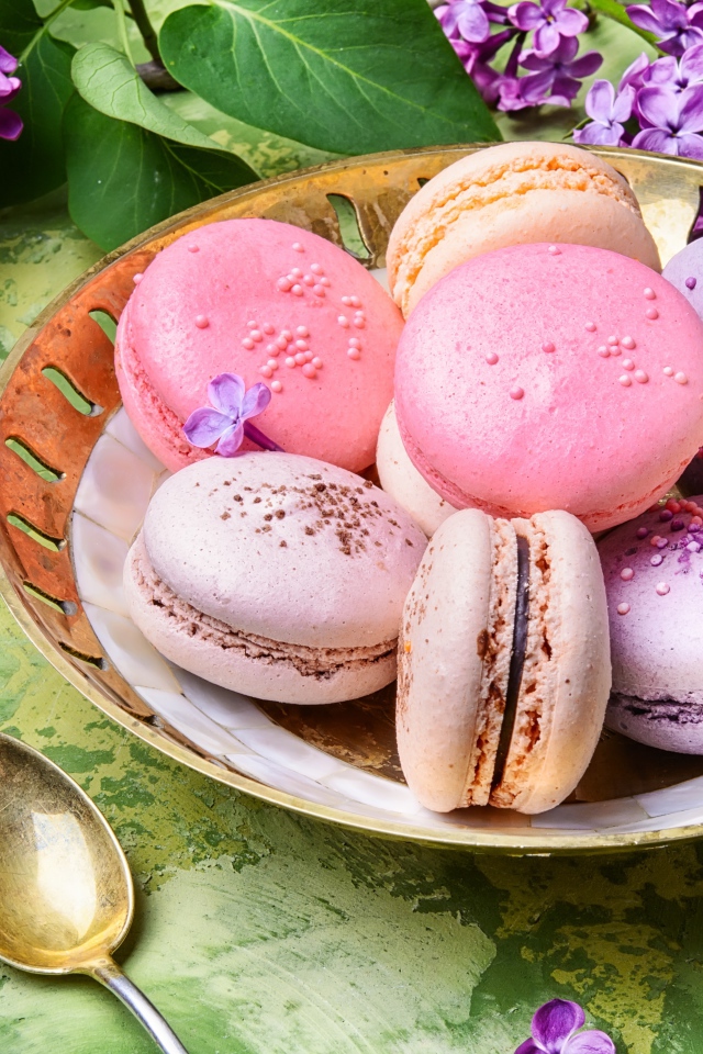 Разноцветный десерт макарон в тарелке на столе с цветами сирени 