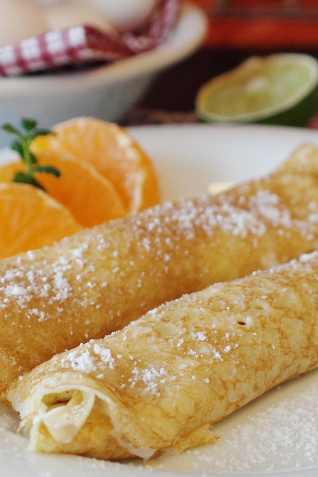 Блины с сахарной пудрой на тарелке с дольками мандарина