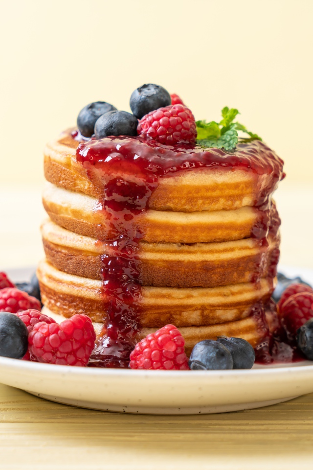 Румяные панкейки с джемом и ягодами черники и малины на тарелке