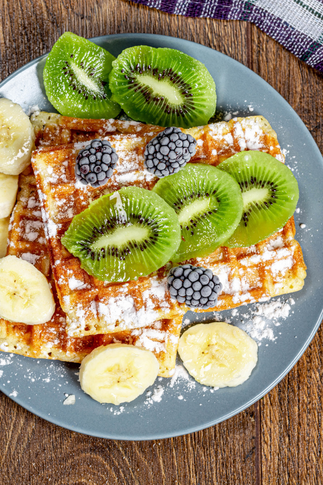 Сладкие вафли на тарелке с сахарной пудрой, бананами и киви