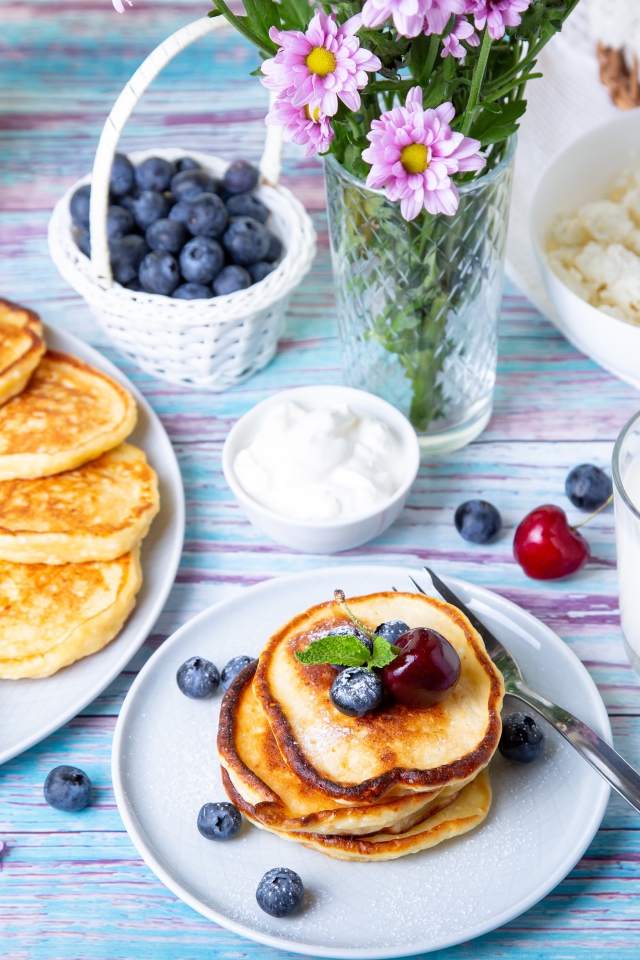 Вкусные оладьи на столе с ягодами черники, творогом и молоком