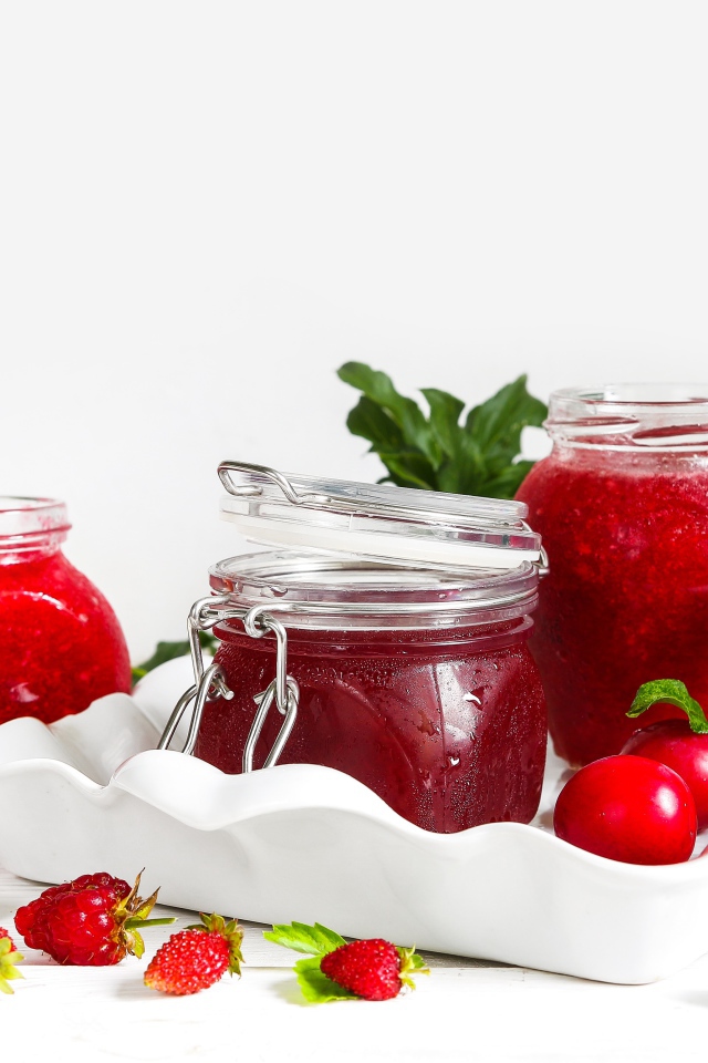 Три банки джема с ягодами на белом фоне