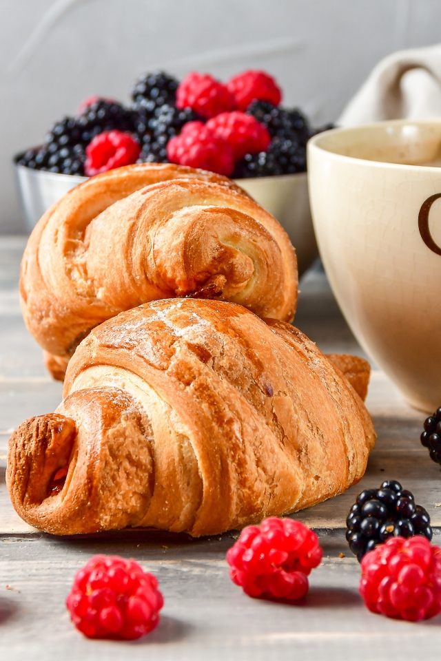 Два круассана с малиной, черникой и чашкой кофе на столе