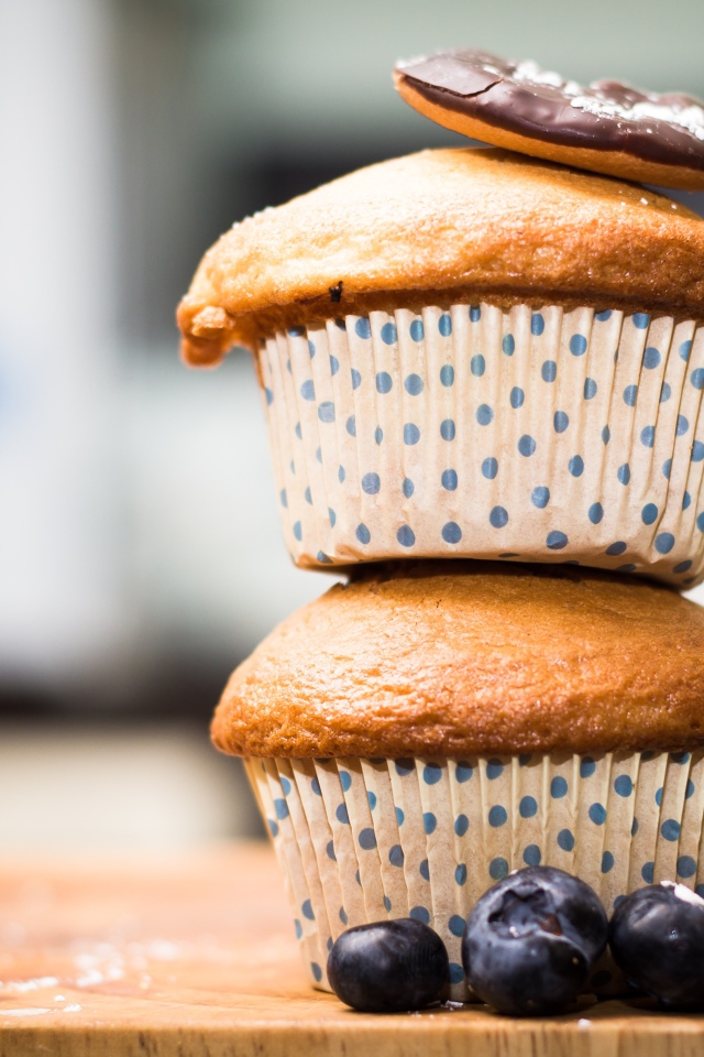 Два кекса стоят на столе с ягодами черники 