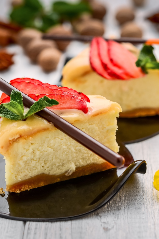 Два куска чизкейка с клубникой на столе с палочками