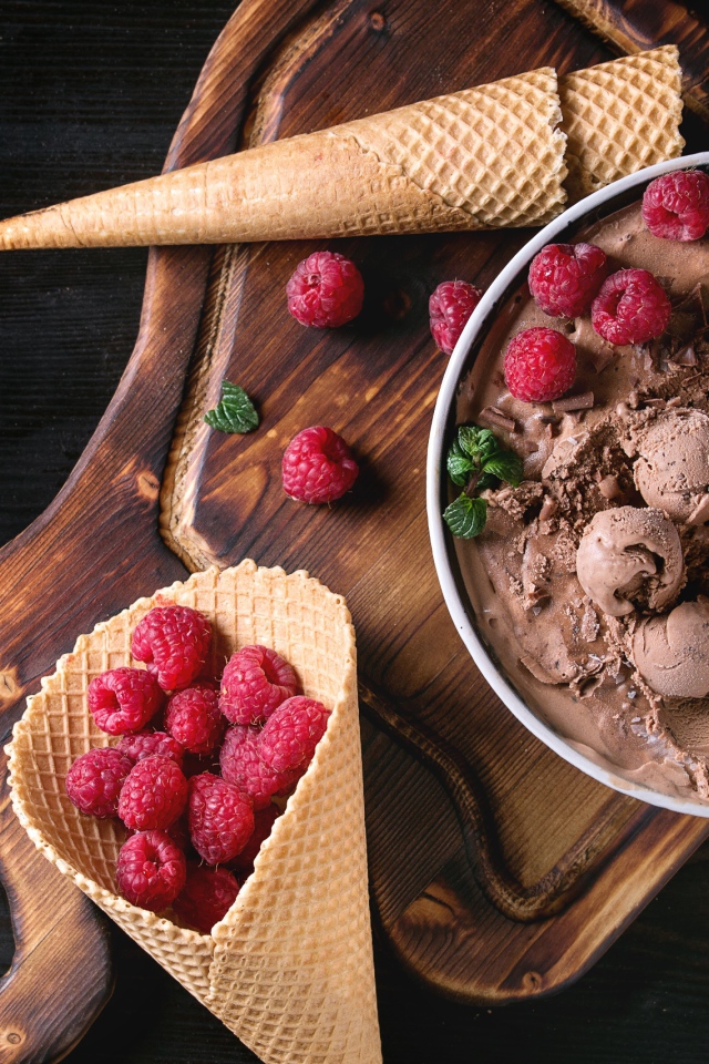 Вафельный рожок с шоколадным мороженым и ягодами малины на столе
