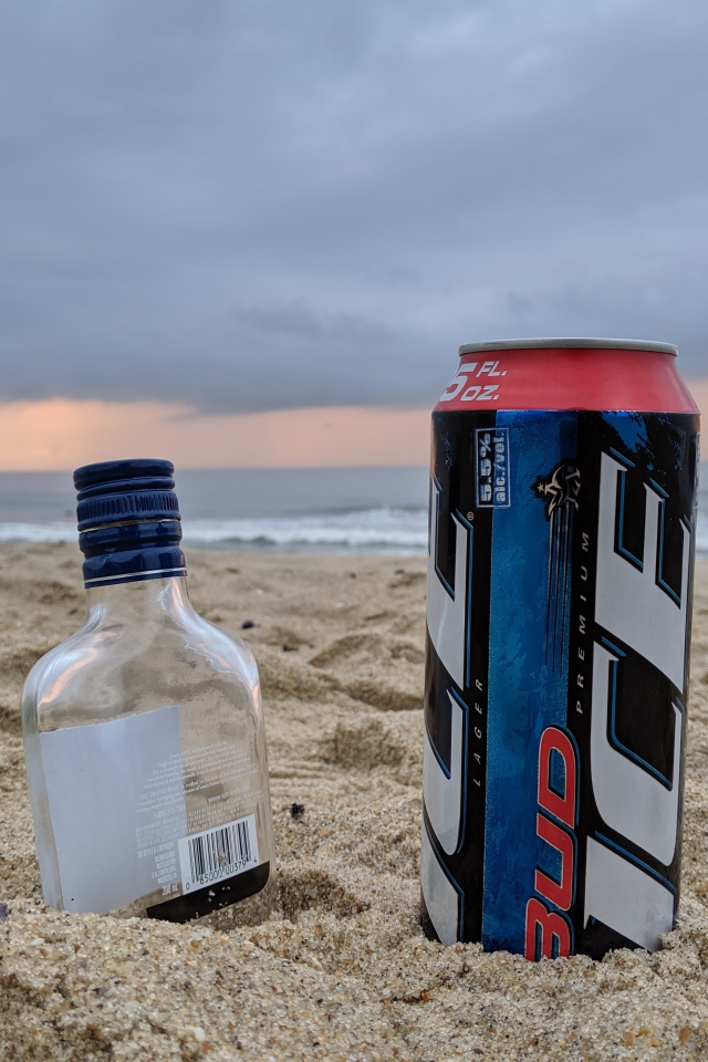 Бутылка пива и бутылка водки на песке у моря