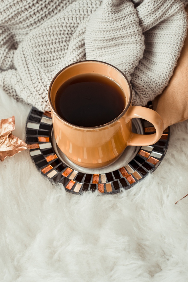 Чашка кофе стоит на покрывале с теплым свитером 