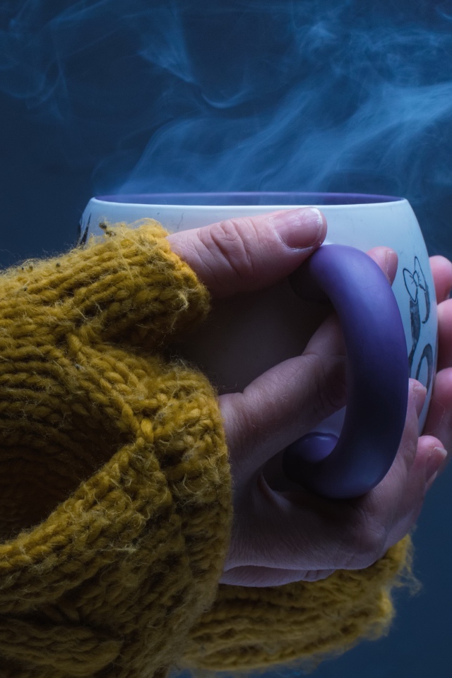 Чашка горячего кофе в руках у девушки на сером фоне