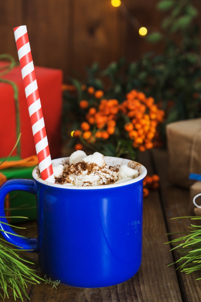 Синяя чашка горячего шоколада с маршмеллоу на столе с еловыми ветками и подарками