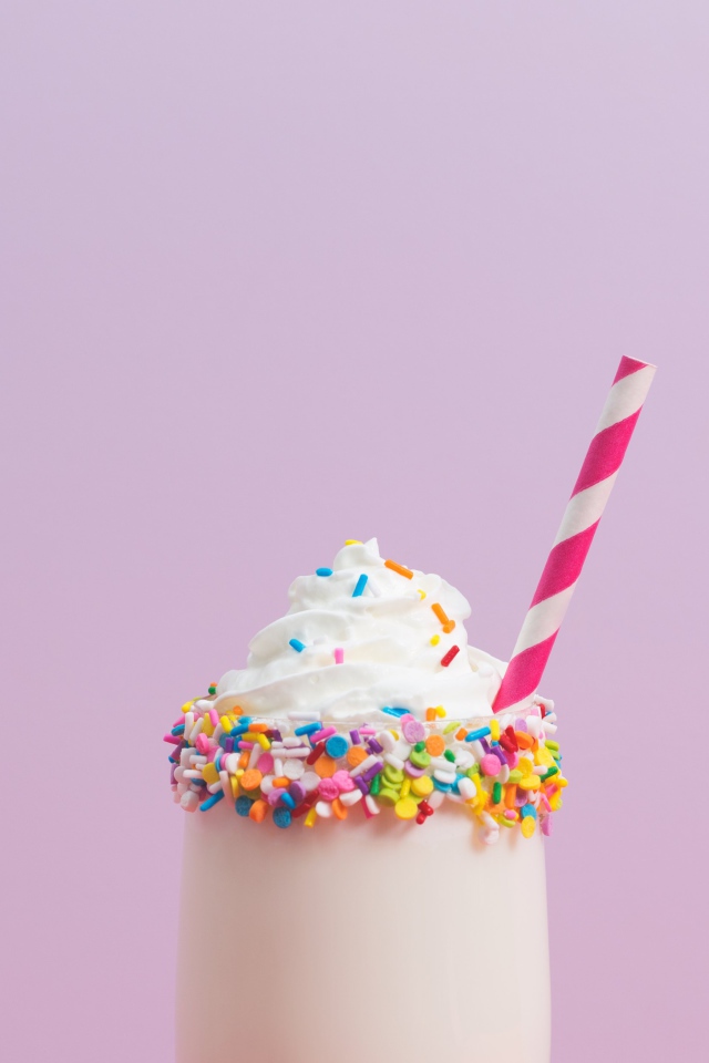 Коктейль  в стакане со взбитыми сливками на розовом фоне