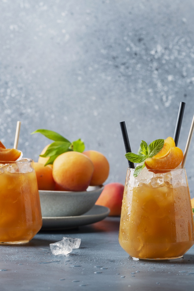 Холодный абрикосовый напиток со льдом в стаканах на столе со свежими абрикосами