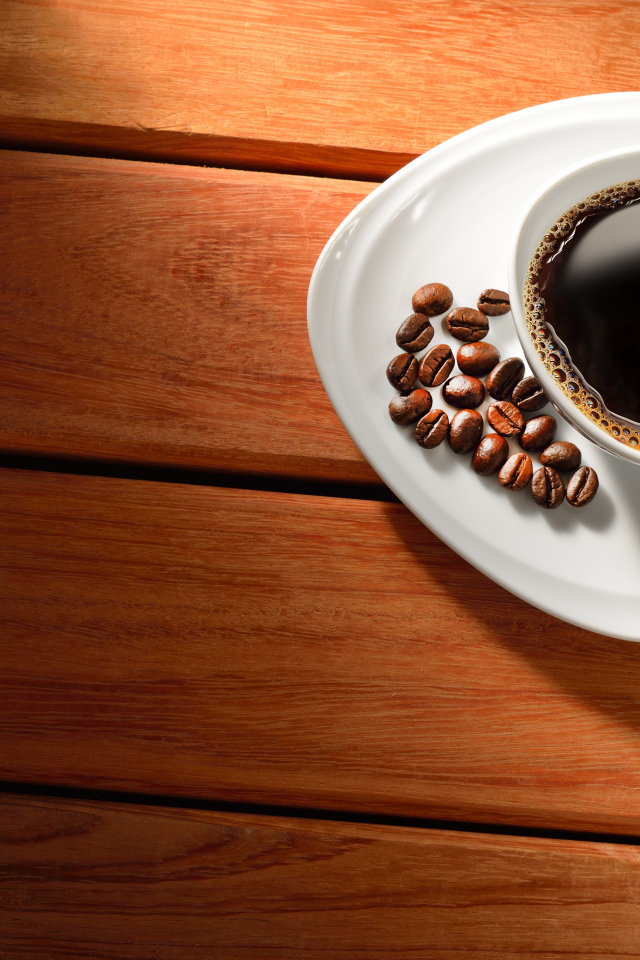 Чашка кофе на тарелке с зернами на деревянном столе