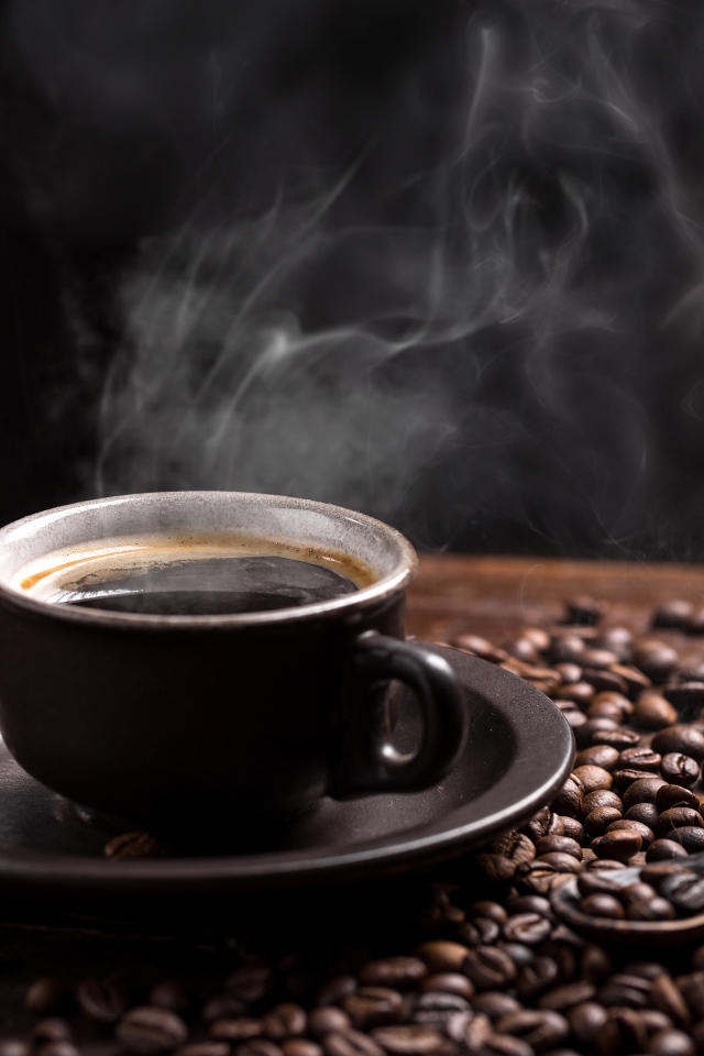 Чашка горячего ароматного кофе на столе с зернами и ложкой