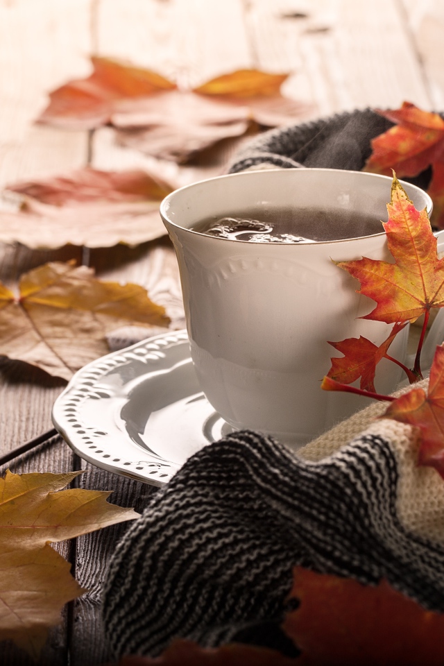 Чашка чая на столе с осенними листьями и пледом