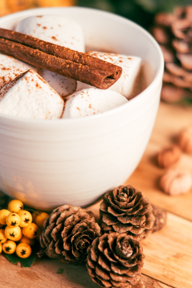 Маршмеллоу в чашке с корицей на столе с шишками и гроздьями рябины