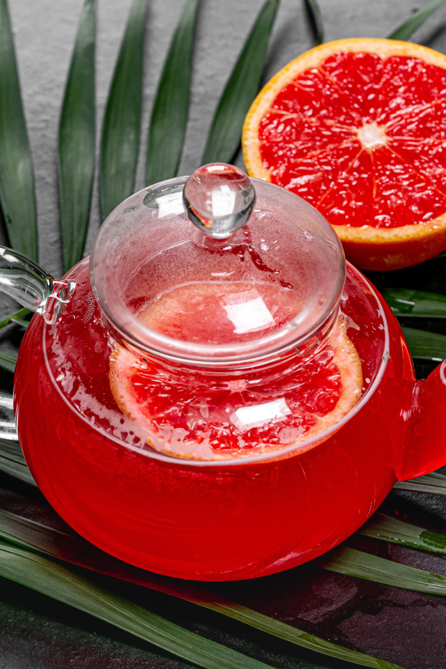 Красный чай в чайнике на столе в грейпфрутом и листьями