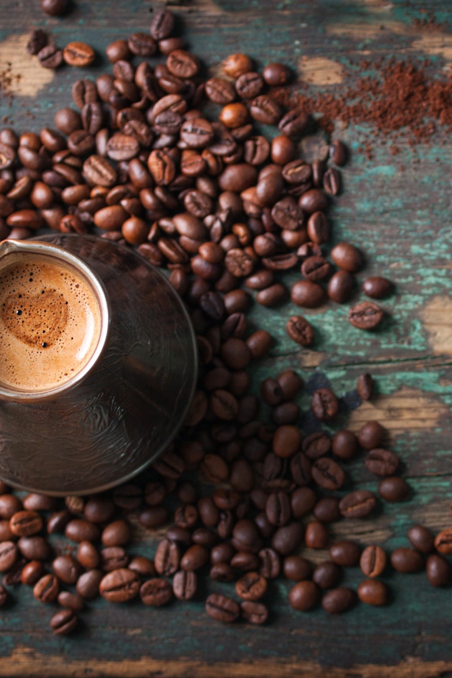 Турка с кофе на столе с зернами и зелеными листьями