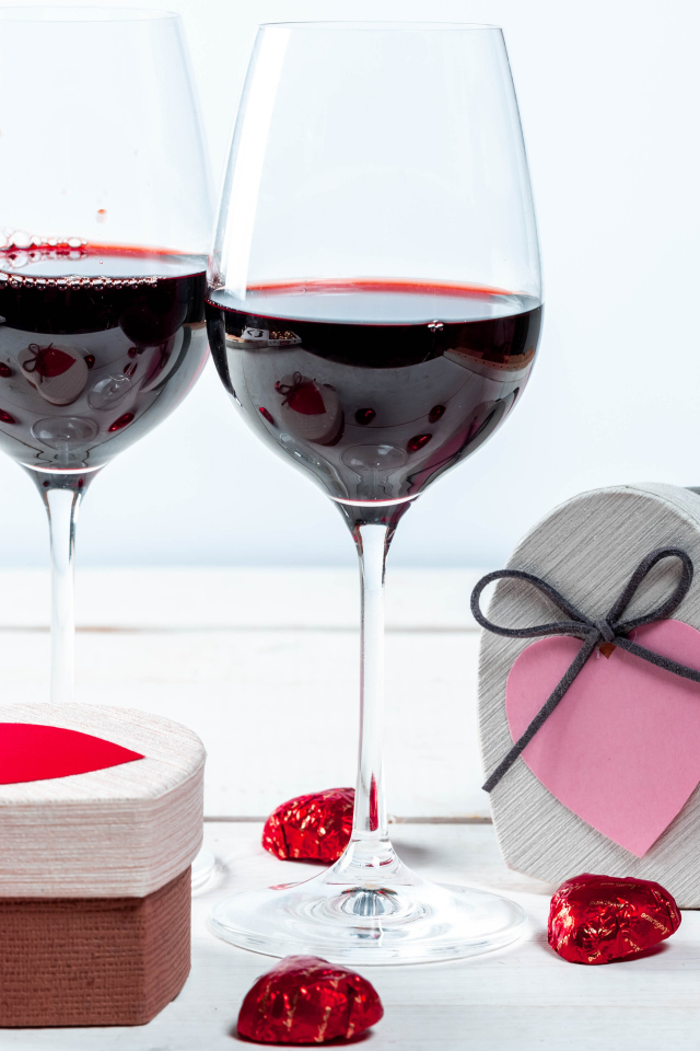 Две коробки с конфетами в форме сердца на столе с бокалами 