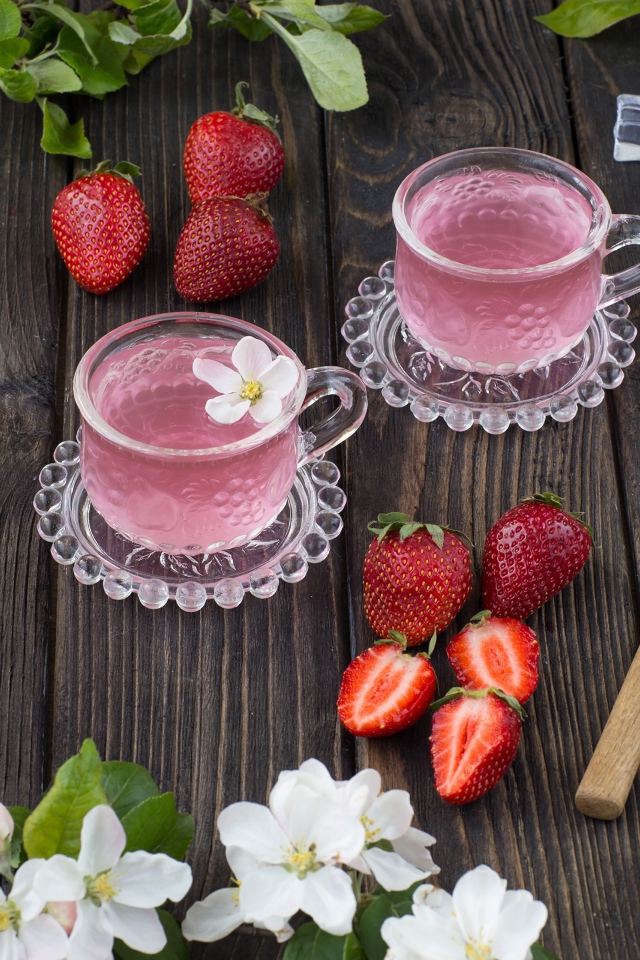 Две стеклянные чашки ягодного чая на столе с клубникой и цветами яблони