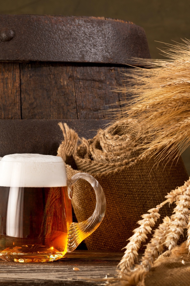 Два бокала пива на столе с колосьями пшеницы  и бочкой
