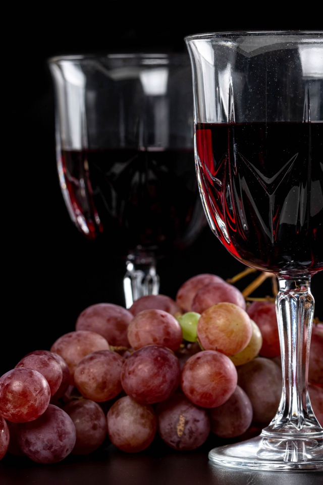 Two glasses of wine on a black background with grapes