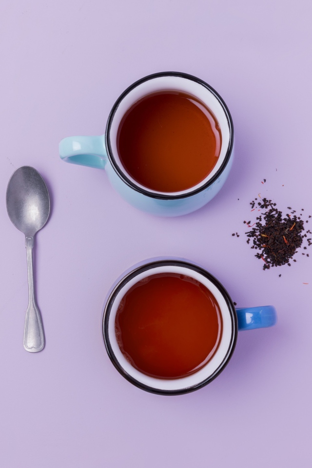 Две железные чашки чая на сиреневом фоне с ложкой