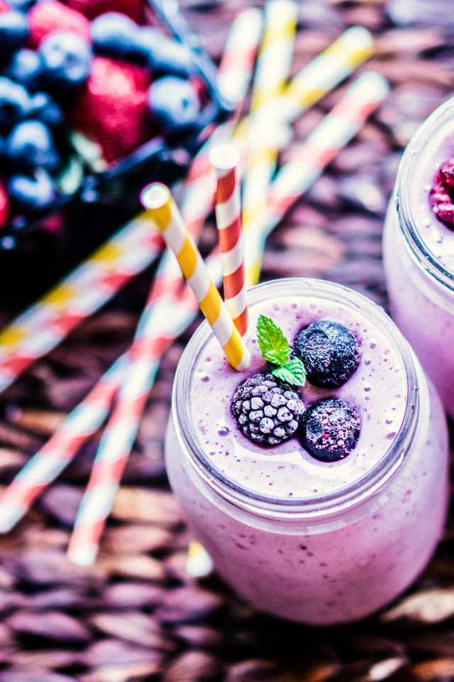 Две банки смузи с трубочками на столе с ягодами