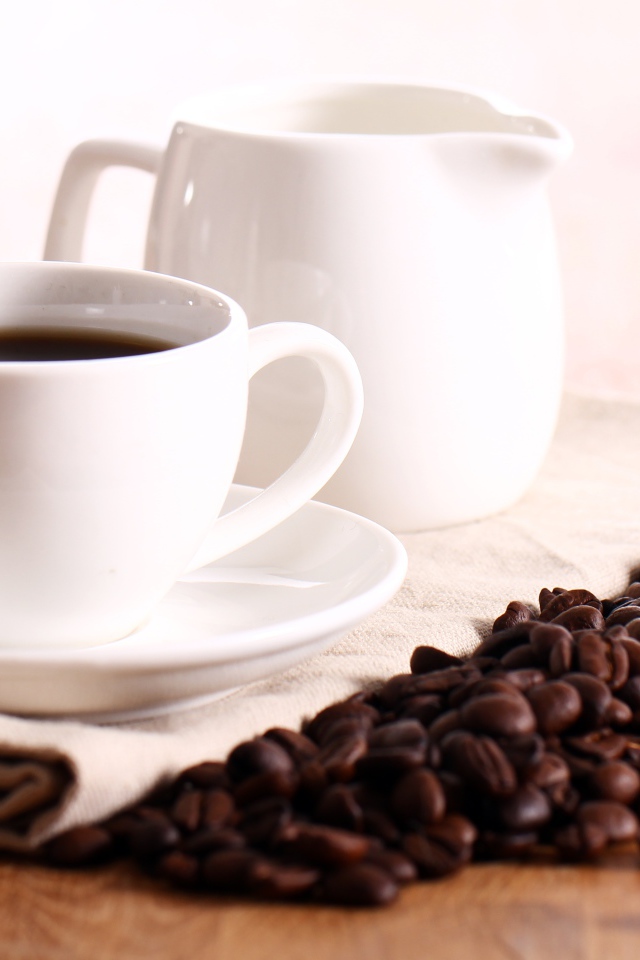 Белая чашка кофе на столе с молоком и зернами