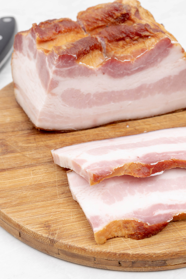 Кусок вкусного копченого сала на доске с ножом