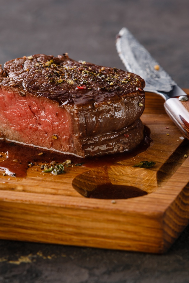 Кусок сочного мяса на доске с ножом и вилкой 