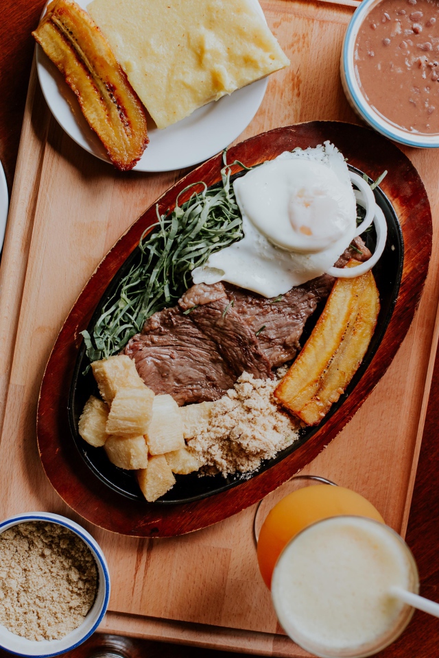 Кусок мяса в жаровне на столе с напитками, овощами и рисом