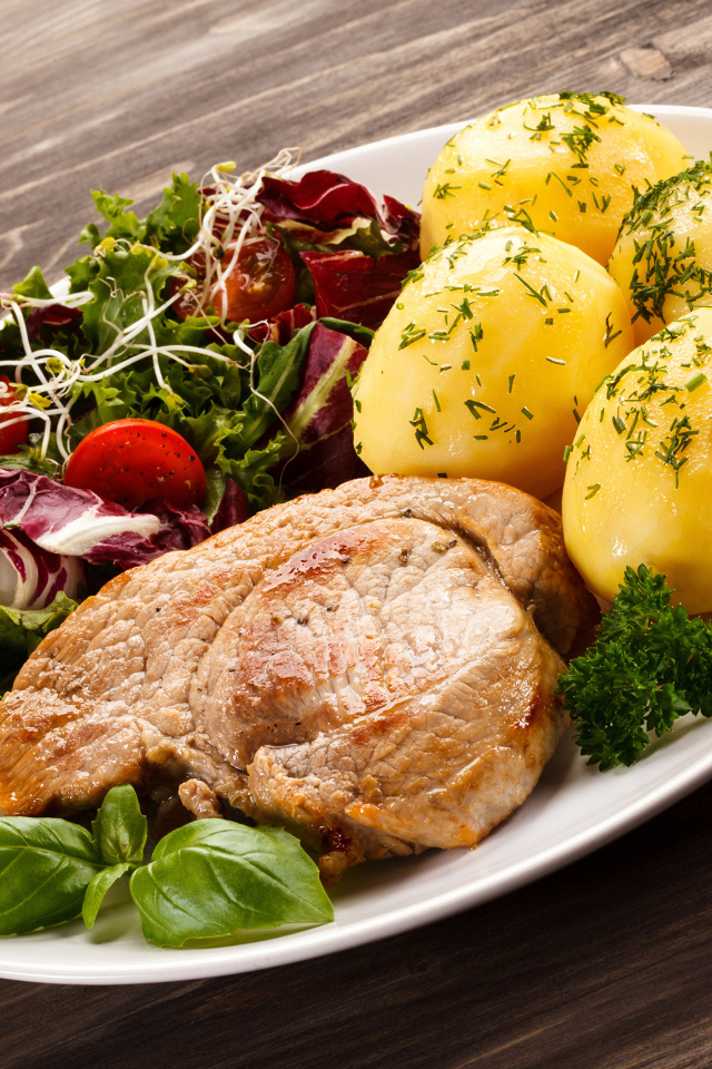 Кусок мяса на тарелке с картофелем и салатом