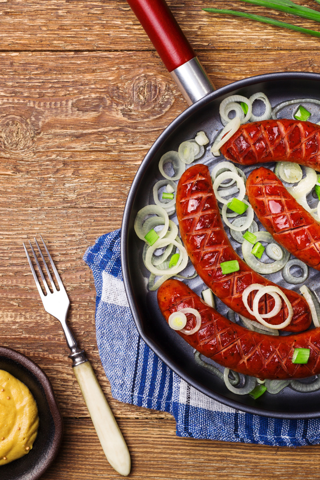 Колбаски барбекю с луком на сковороде на столе с соусом