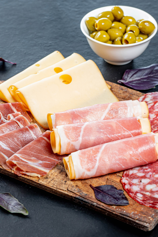 Сыр, бекон и колбаса на разделочной доске на столе с оливками