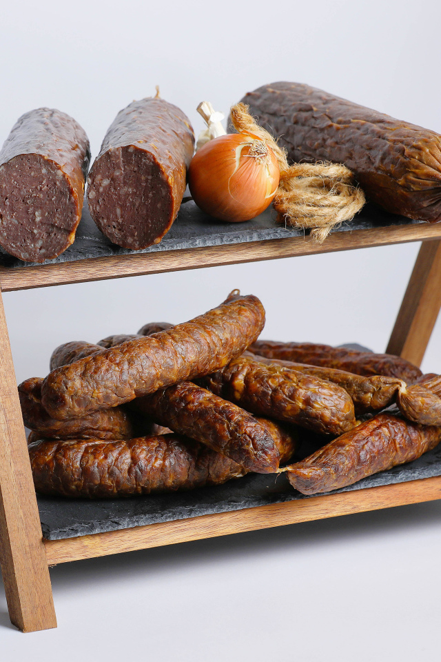 Различные виды колбасы на полке с луком на сером фоне