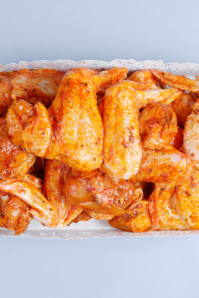 Жареные куриные крылья в белой корзине на сером фоне