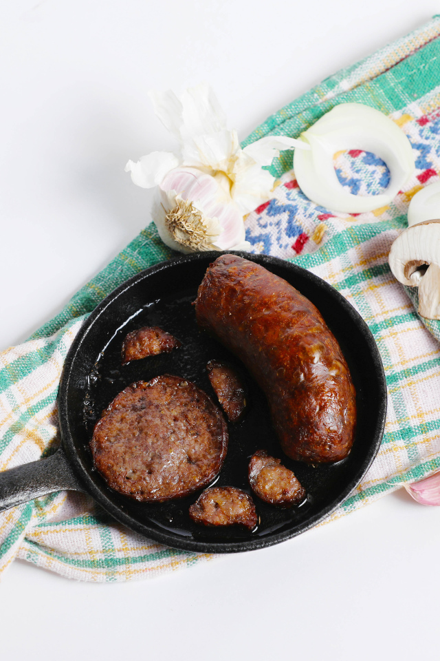 Сковорода с жареной колбасой на столе с полотенцем и чесноком