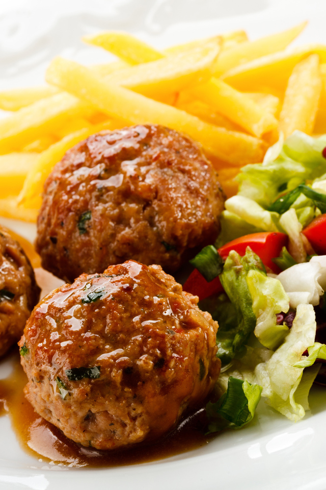 Фрикадельки с салатом и картофелем фри на белой тарелке