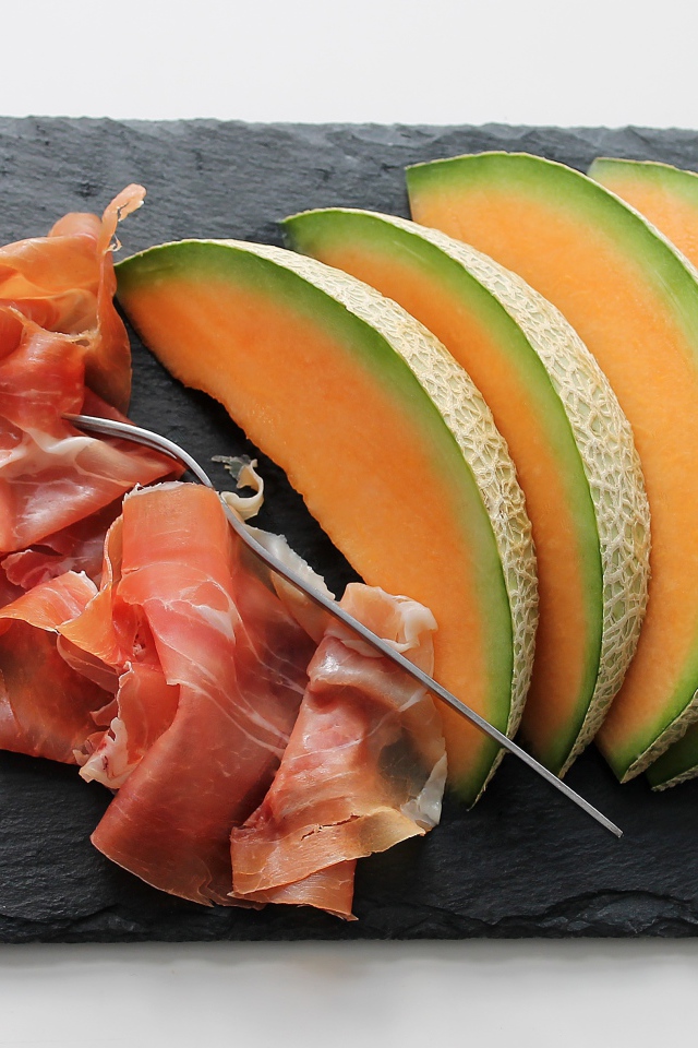 Кусочки дыни на доске с прошутто