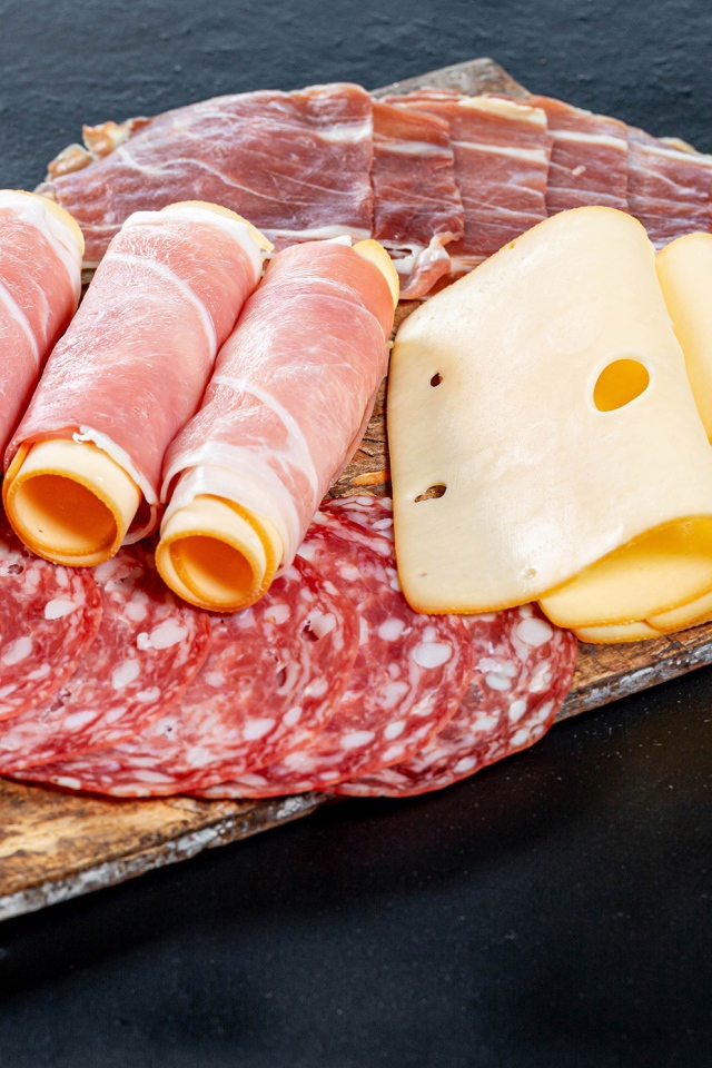 Куски сыра, ветчины и колбасы на доске