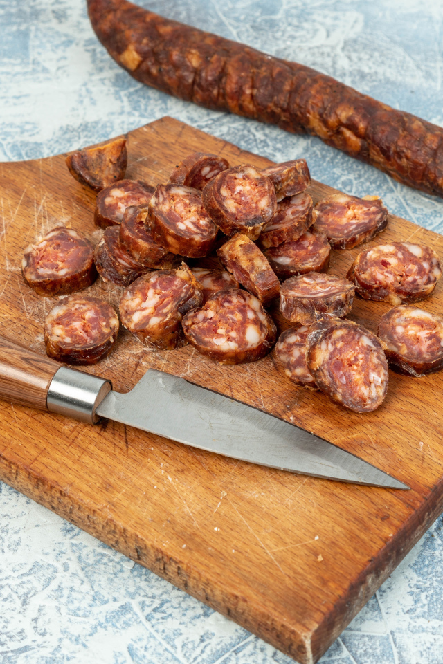 Колбаса нарезана колечками на разделочной доске с ножом 