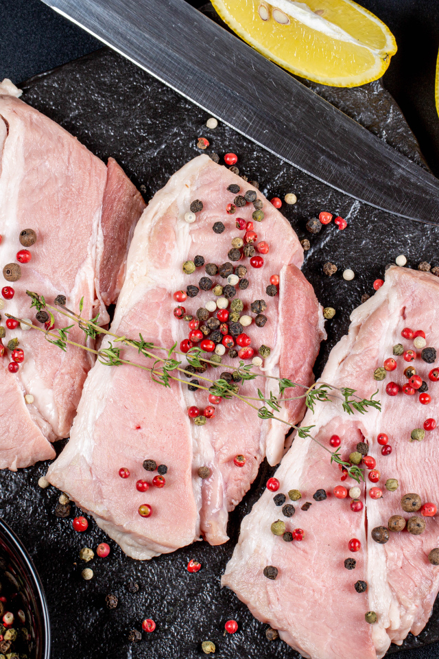 Куски свежего мяса на столе с зернами перца и лимоном