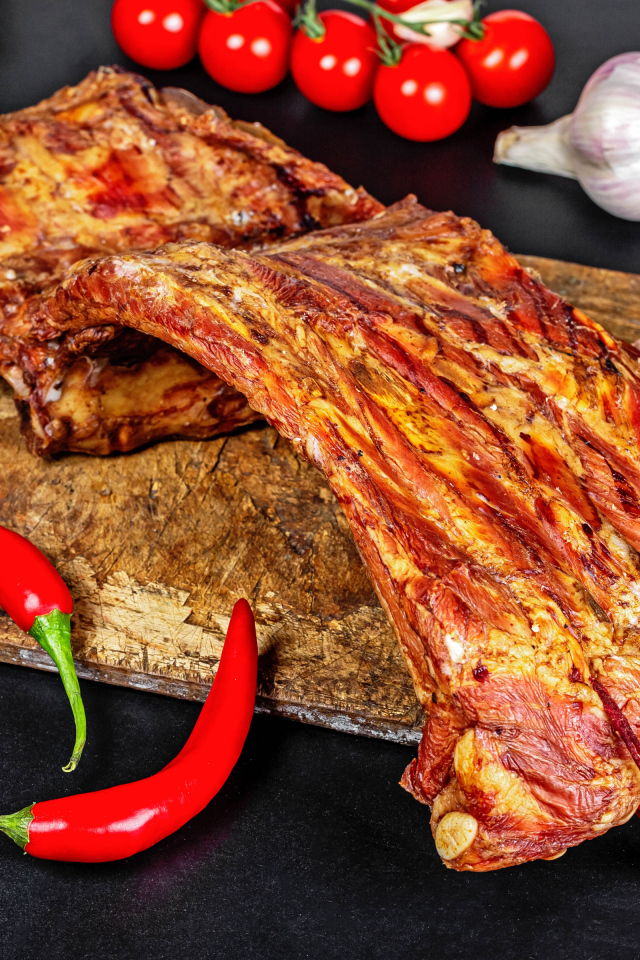 Копченые ребра на столе с красным перцем, чесноком и помидорами