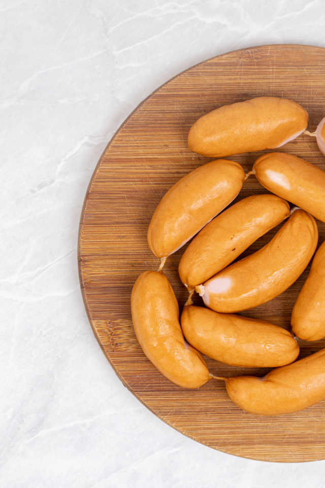 Копченые сардельки на деревянной доске на сером фоне