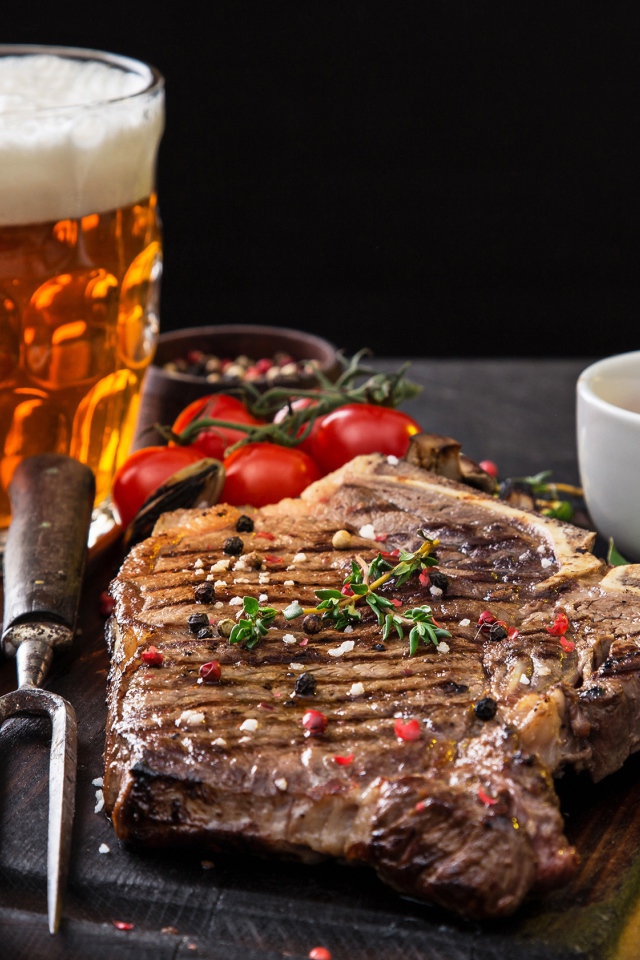 Вкусный кусок мяса на столе с помидорами и бокалом пива